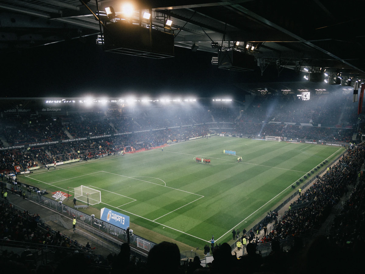 Floodlit football stadium at night, packed stands and pitch in fine Ultra HD detail